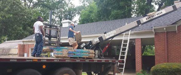 A man is standing on the back of a truck with a crane attached to it