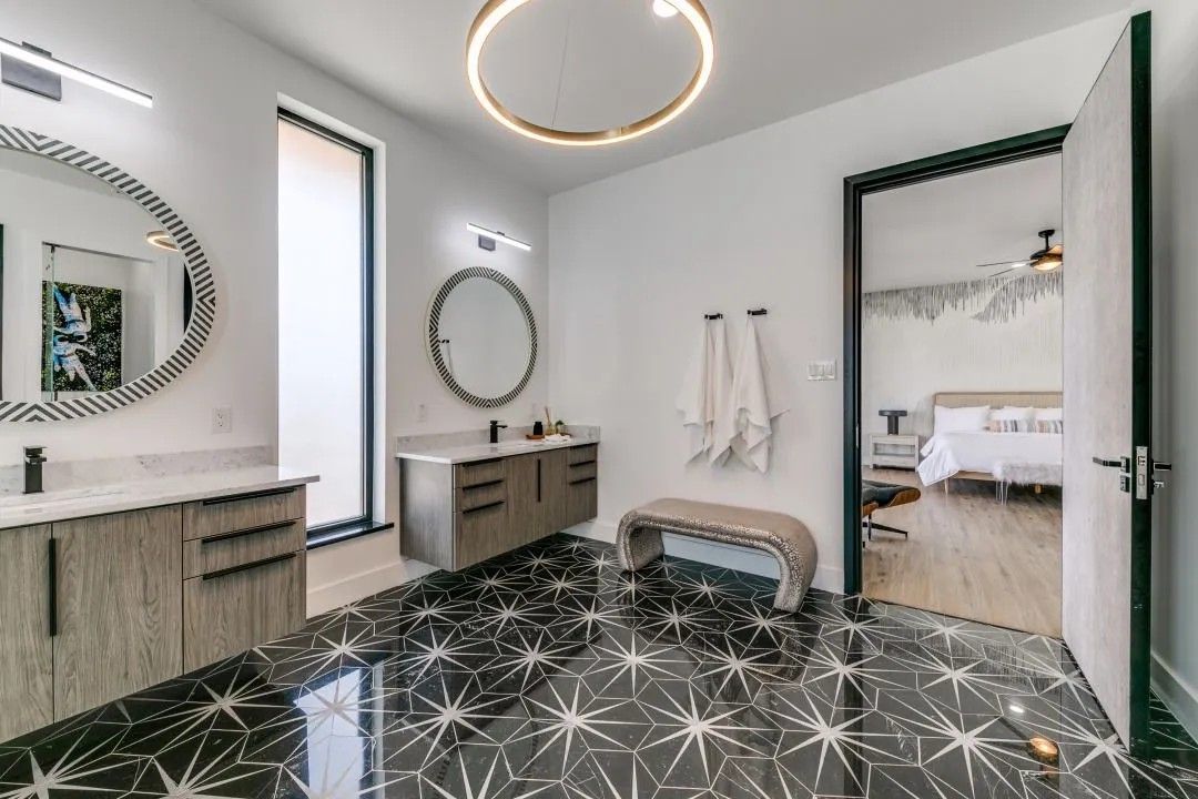 Modern bathroom with black and white starburst tile floor, floating wood vanities, and open doorway to a bedroom.
