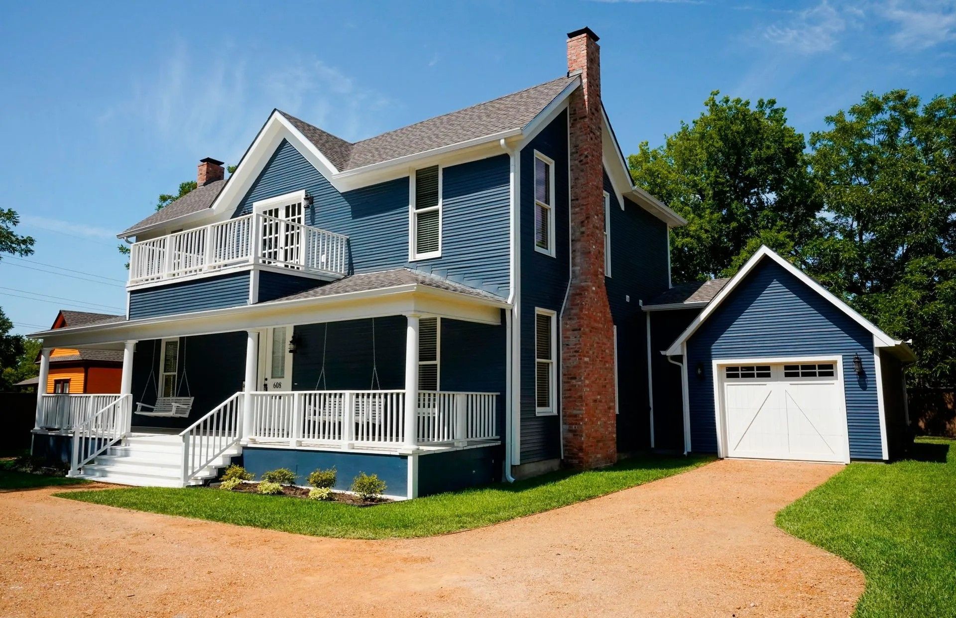Blue two-story house with a porch and attached garage, brown gravel driveway, blue sky.