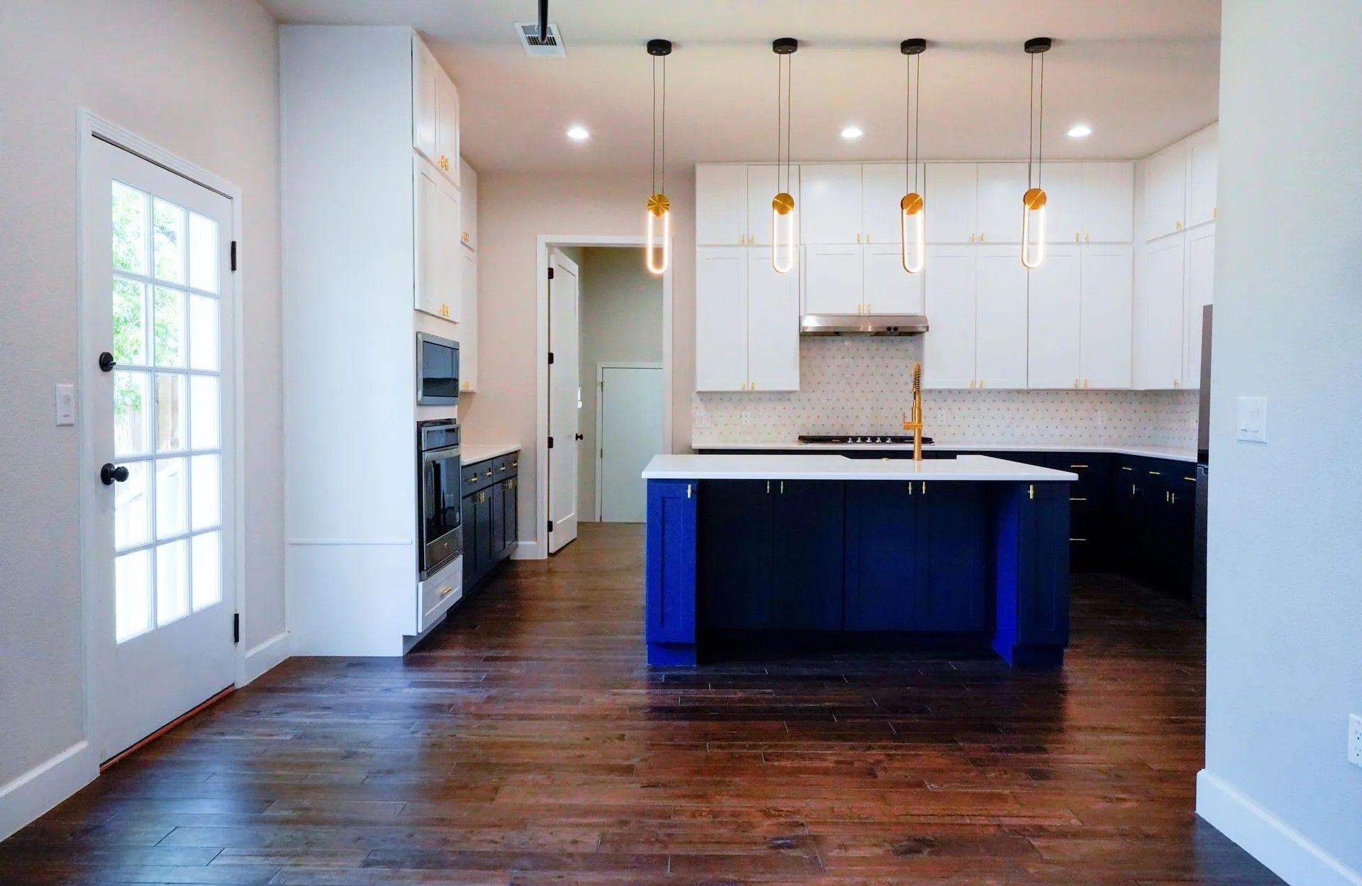 Modern kitchen with dark blue island and white cabinets. Wooden floor, pendant lights, and a door to the left.