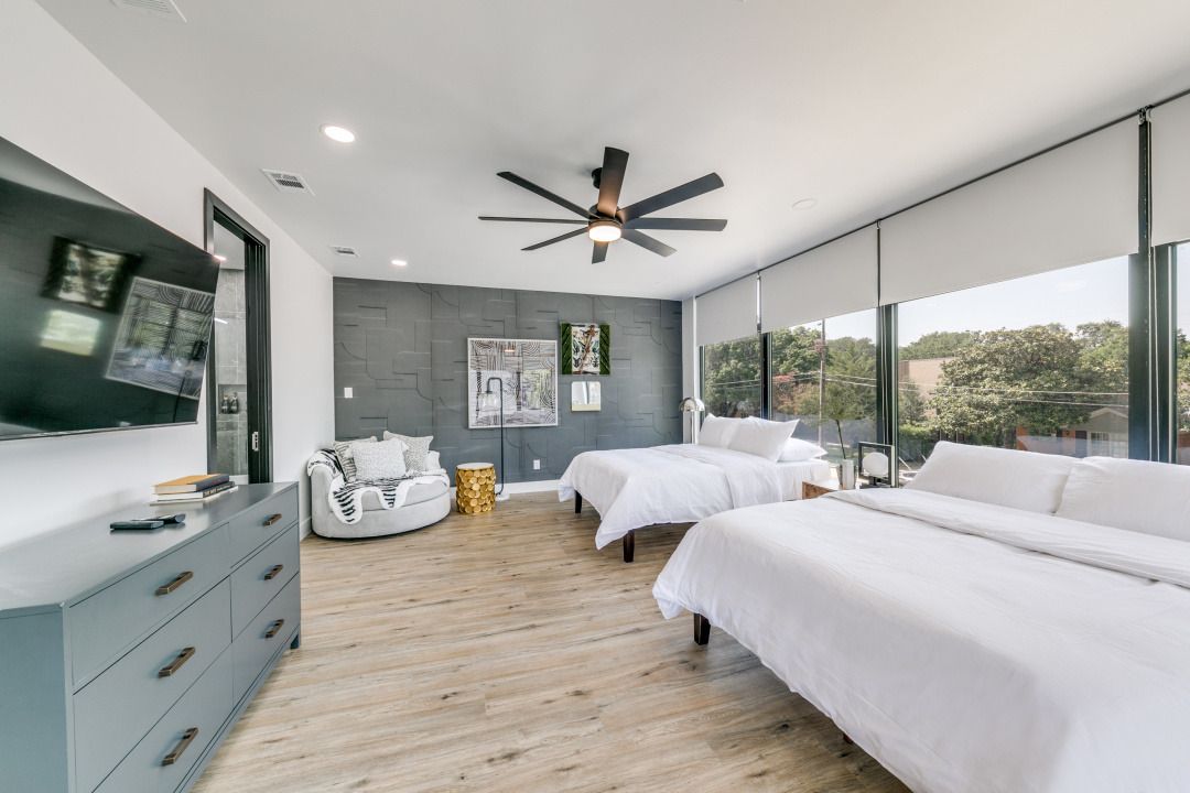 Spacious bedroom with two beds, a dresser, a TV, and a seating area, with large windows offering an outdoor view.