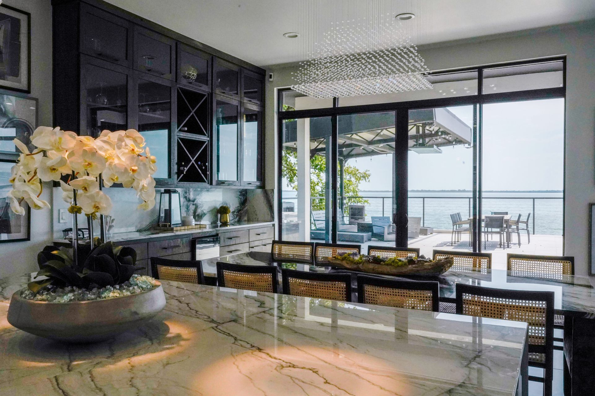 Luxury dining room with a marble island, black cabinetry, and a view of the water. A large orchid arrangement sits on the counter.