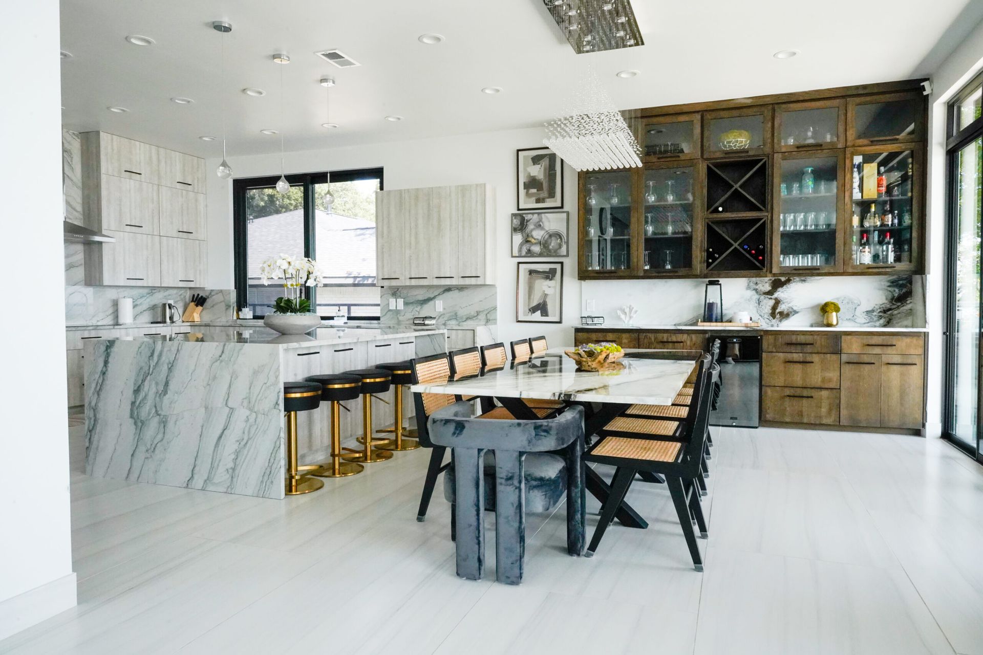 Bright, modern kitchen with white cabinets, marble island, and a dining table. The space is airy with natural light, and accents of wood and gold.