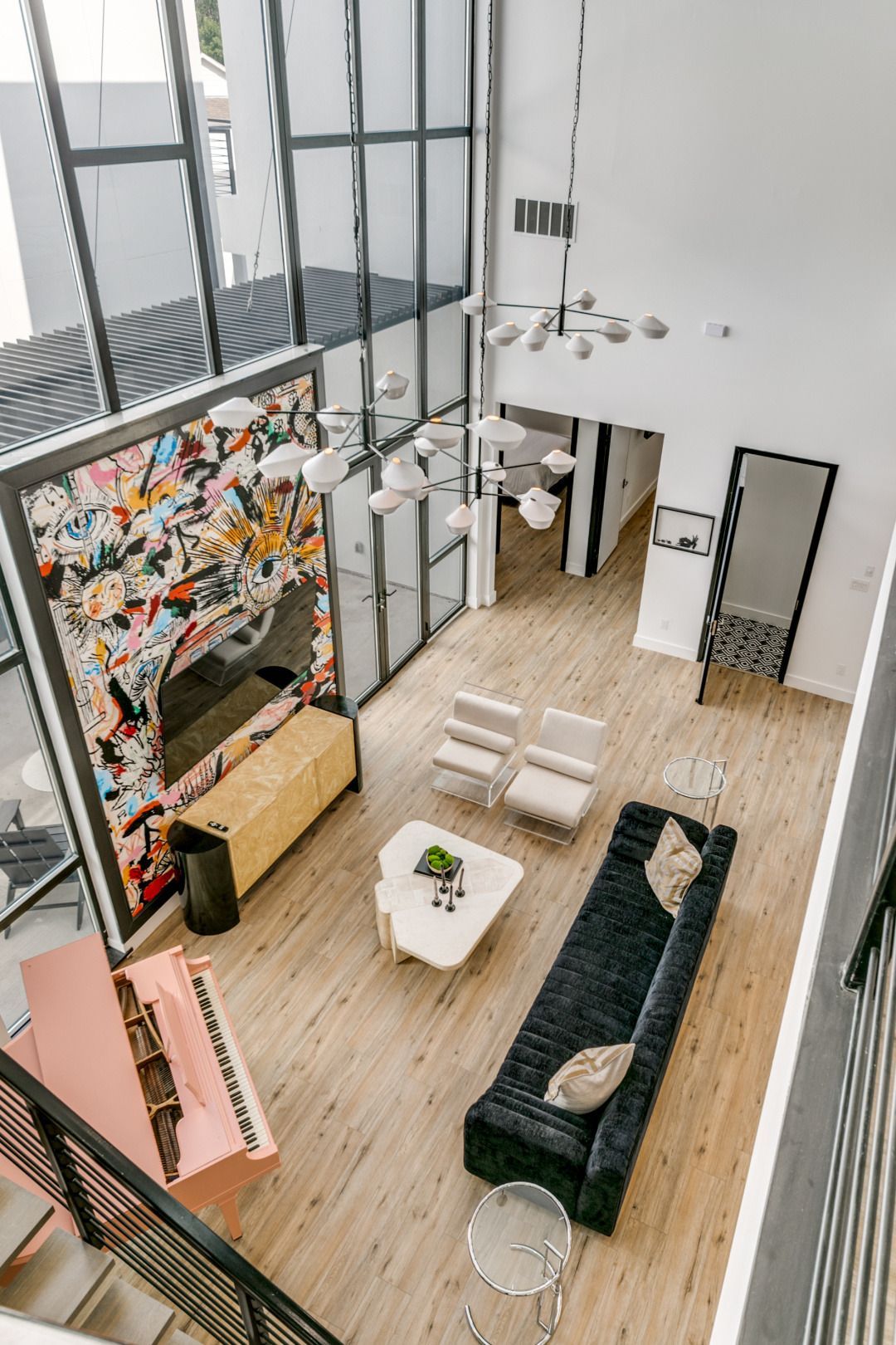 High-angle view of a modern living room with a pink piano, black sofa, and large windows.