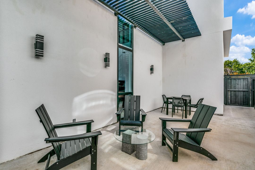 A patio with black Adirondack chairs and a small table, with a dining set in the background.