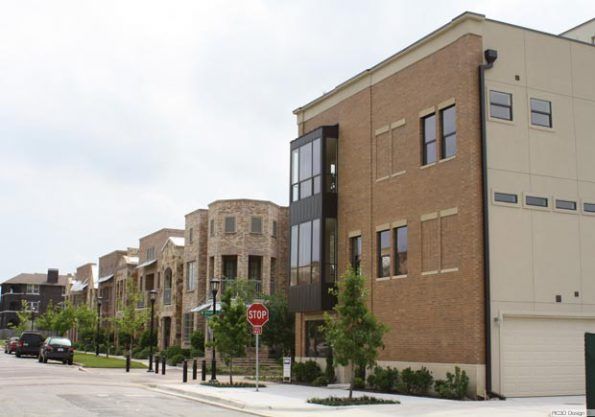 Row of modern brick townhouses on a street, with a stop sign in the foreground and a cloudy sky above.
