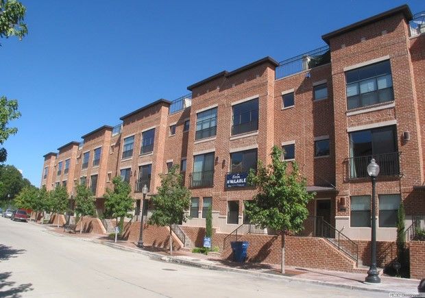 Row of brick townhouses with black framed windows on a sunny day. Sidewalk and trees line the street.