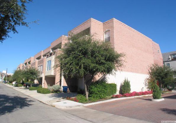 Row of brick townhouses on a sunny street with trees and landscaping.
