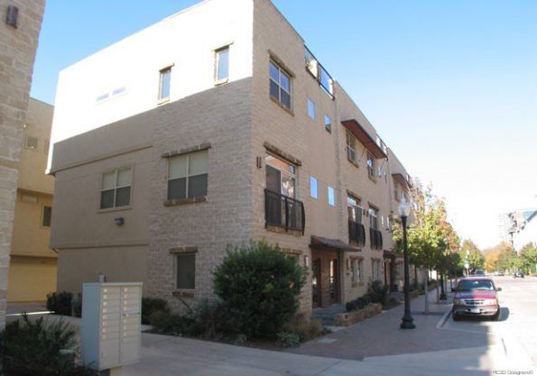 A three-story brick building with balconies and windows, located on a city street with a parked vehicle.