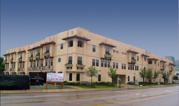 A three-story tan building with Spanish-style architecture; a sign and person are visible on the sidewalk in front.
