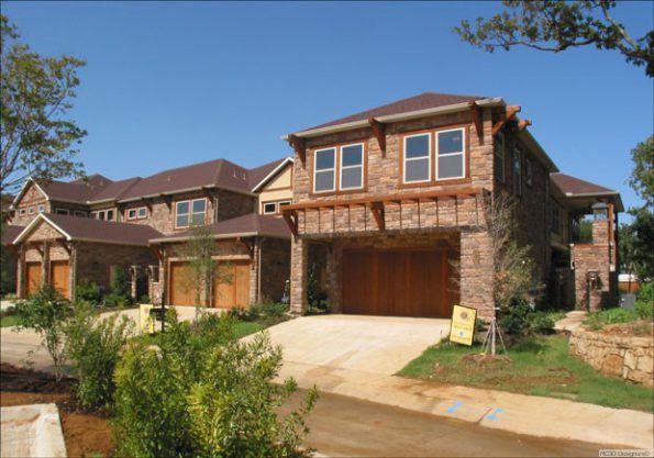 A multi-story brick house with a driveway, garage doors, and a blue sky backdrop.