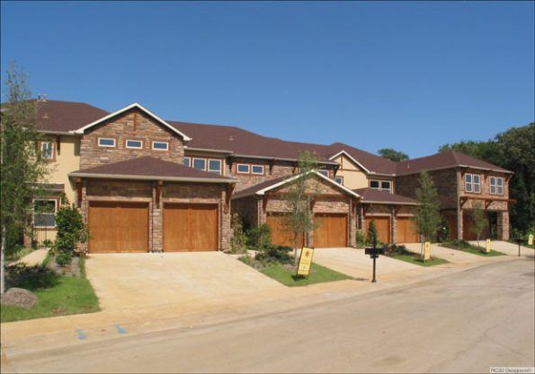Row of attached townhouses with brick and stone exteriors, brown garage doors, and a blue sky.