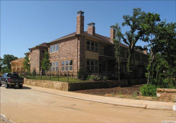 A multi-story brick building with multiple windows and chimneys on a sunny day. A truck is parked on the street in front.