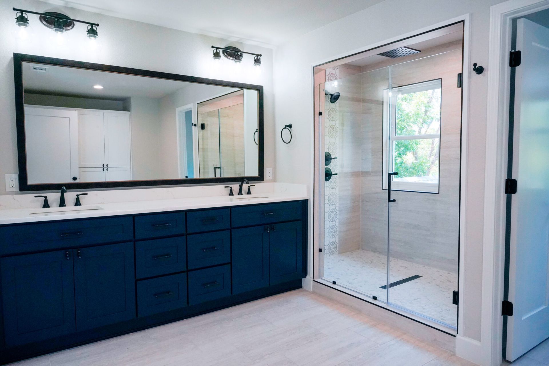 Modern blue bathroom with a large mirror, glass shower, and double vanity.