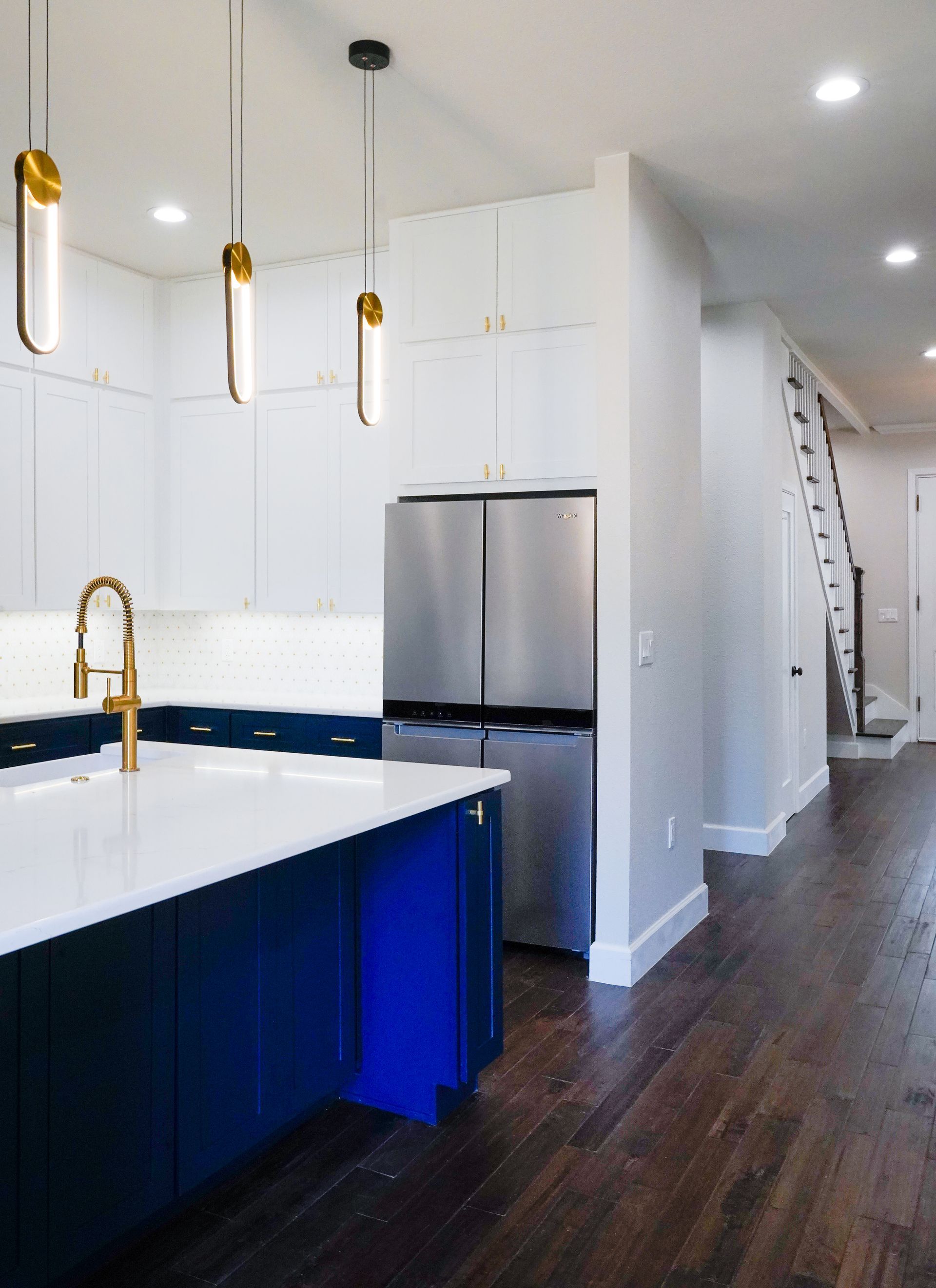 Modern kitchen with white upper cabinets, navy blue island, and stainless steel refrigerator; pendant lights hang over island.