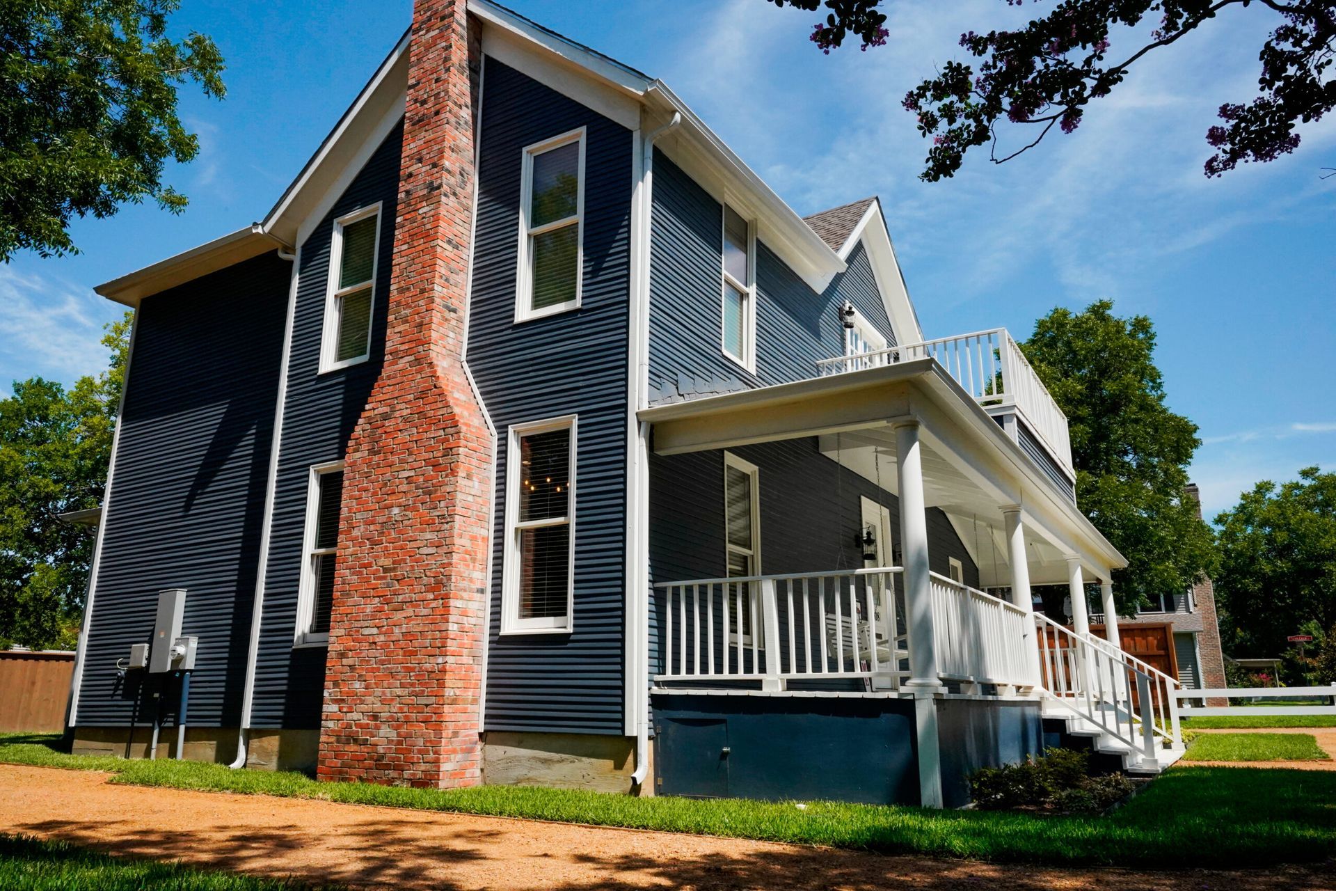 Two-story blue house with white trim and a brick chimney. A white porch wraps around the corner.