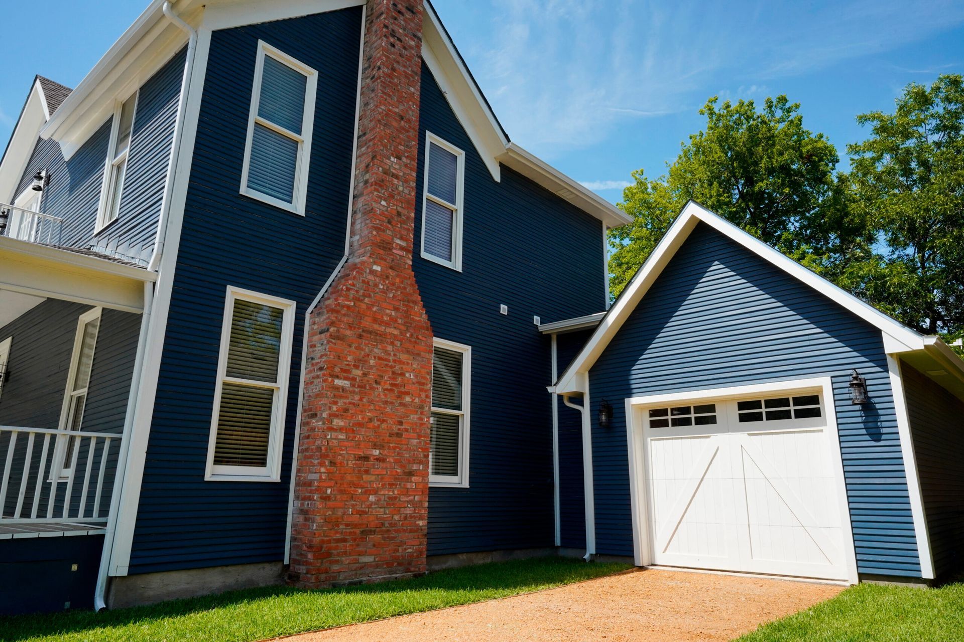 A blue house with a red brick chimney and a white garage door. Green grass and a blue sky are in the background.