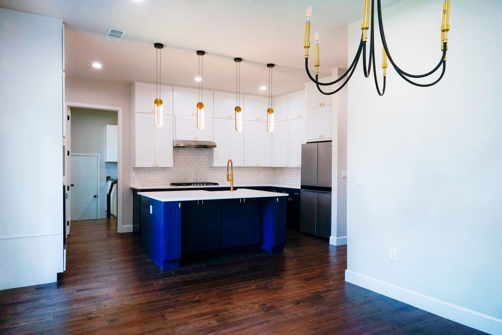 Modern kitchen with blue island and white cabinetry. Overhead pendant lights and a gold chandelier.