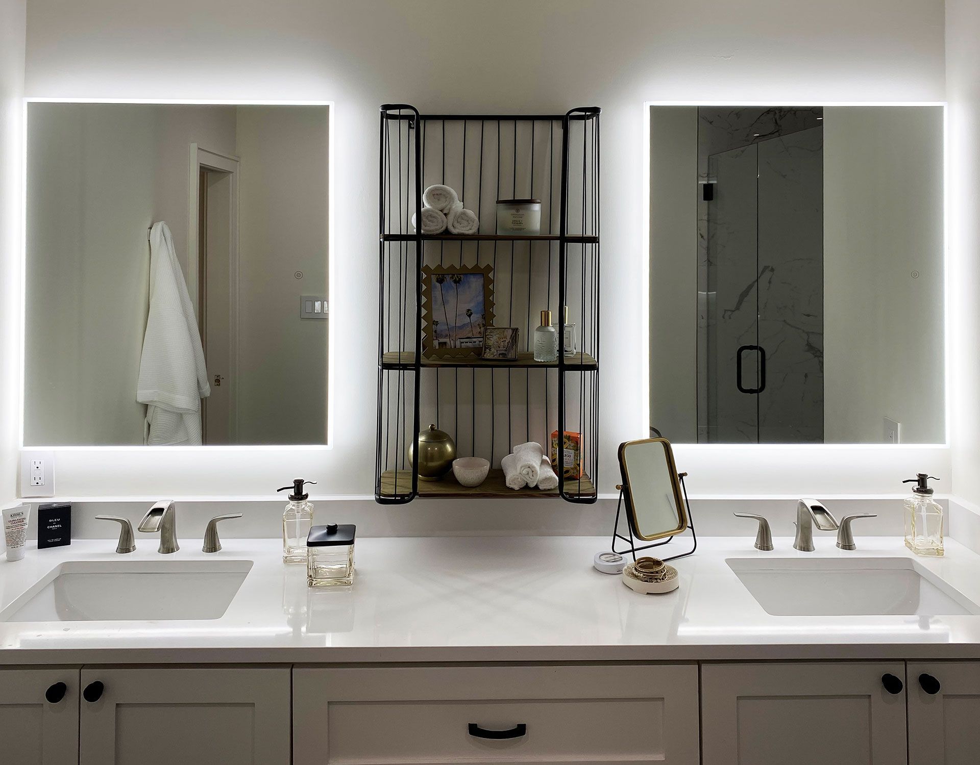 Modern bathroom with two sinks, mirrors with LED lights, and a shelf between them.