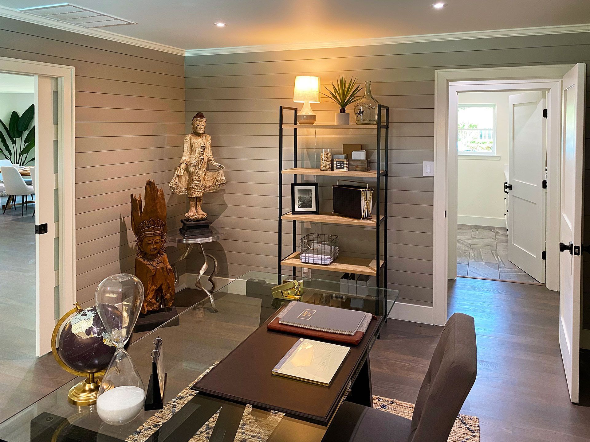Office with desk, shelves, statues, and doors to other rooms; neutral tones.