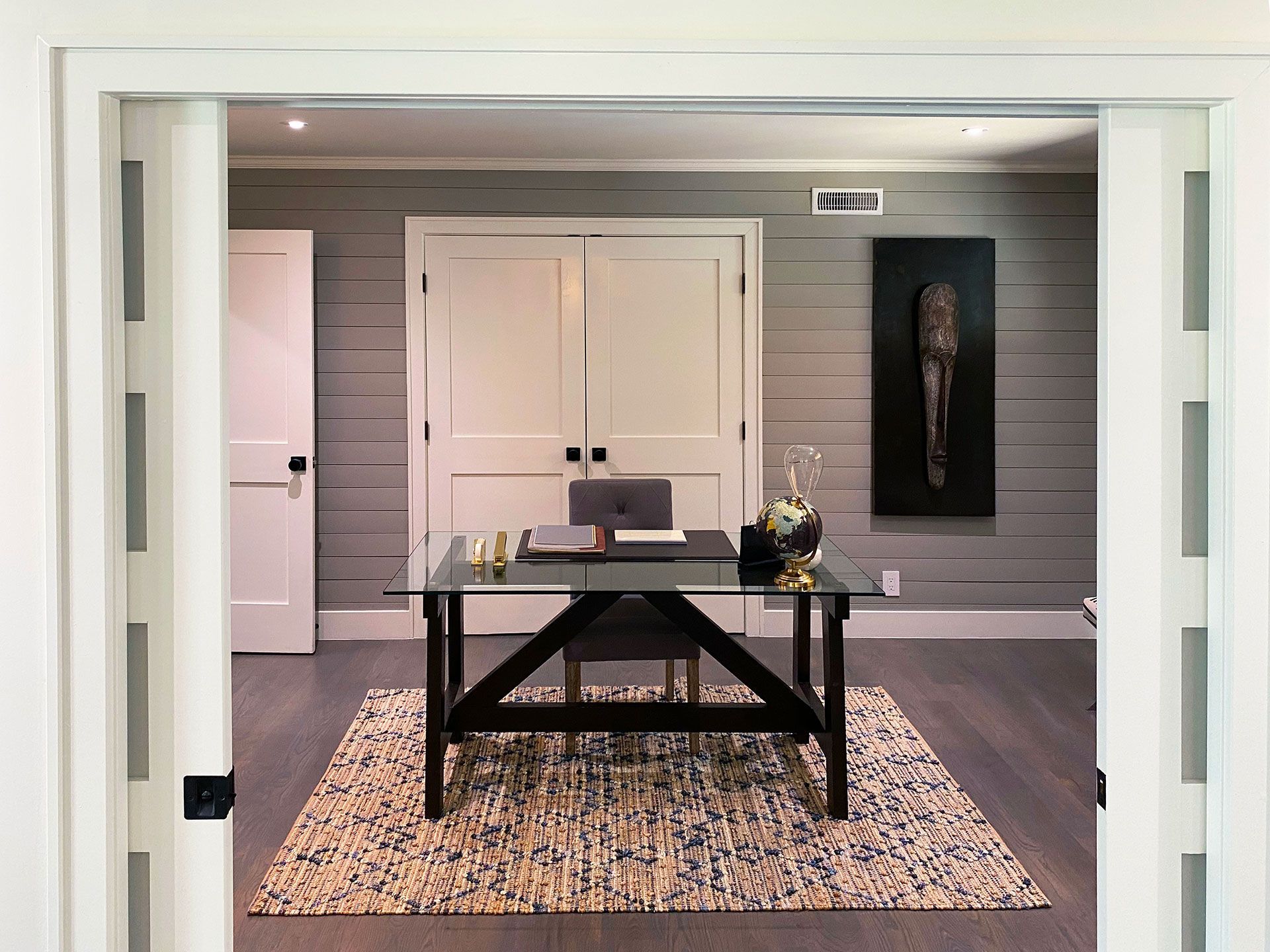 Office with gray plank walls, black desk, rug, and white doors.