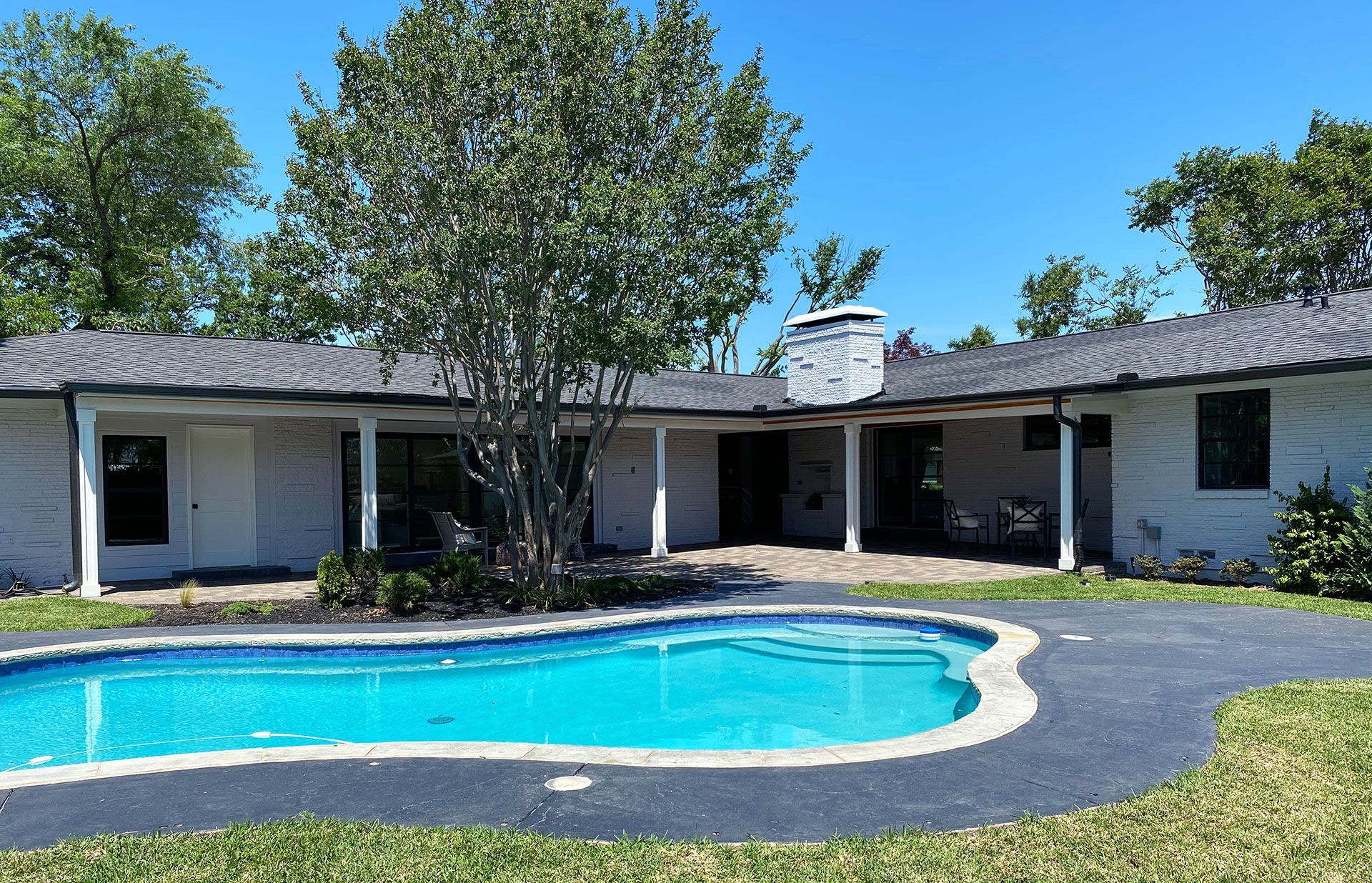 A light-colored, one-story home with a pool and landscaping under a clear, blue sky.