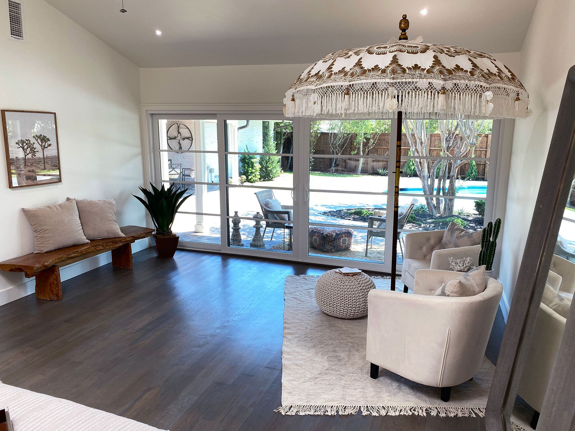 A bright room with a view of a pool area features a bench, armchair, and decorative umbrella.