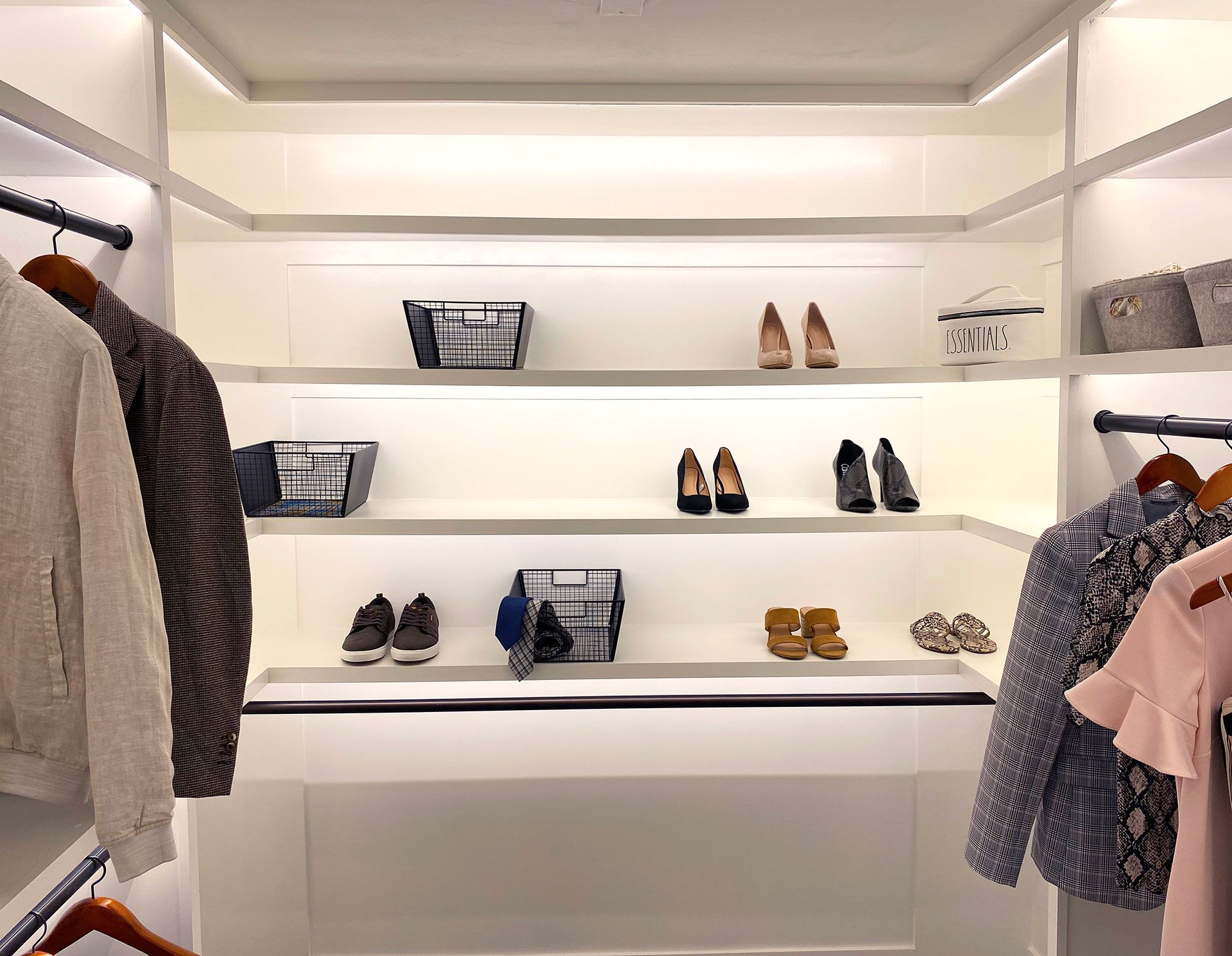 Walk-in closet with illuminated shelves displaying shoes and baskets clothes hang on either side.