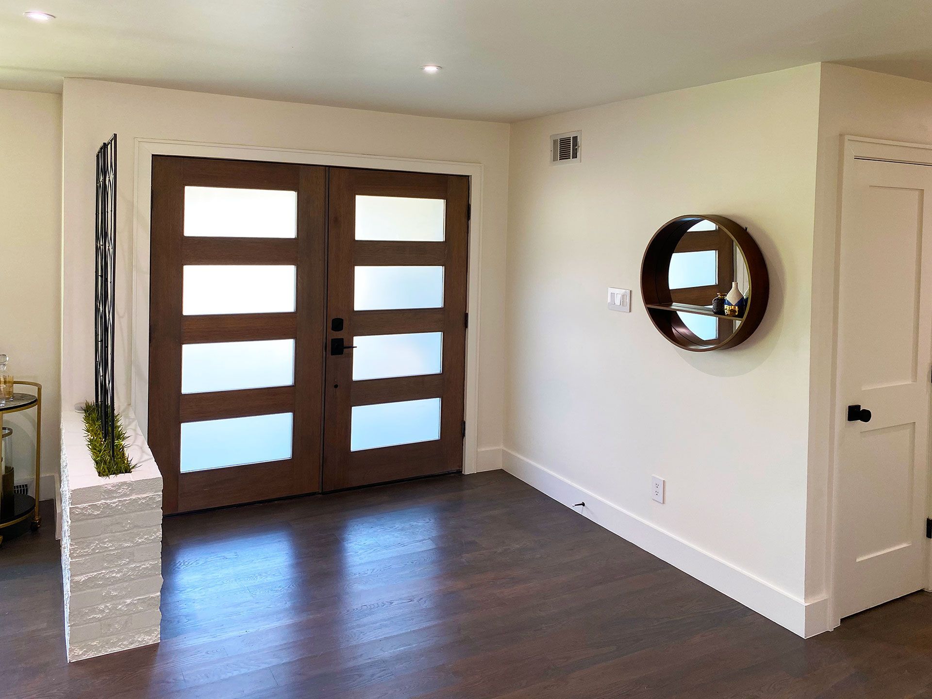 Wooden double doors with frosted glass panels in a neutral hallway, a round mirror on the wall.
