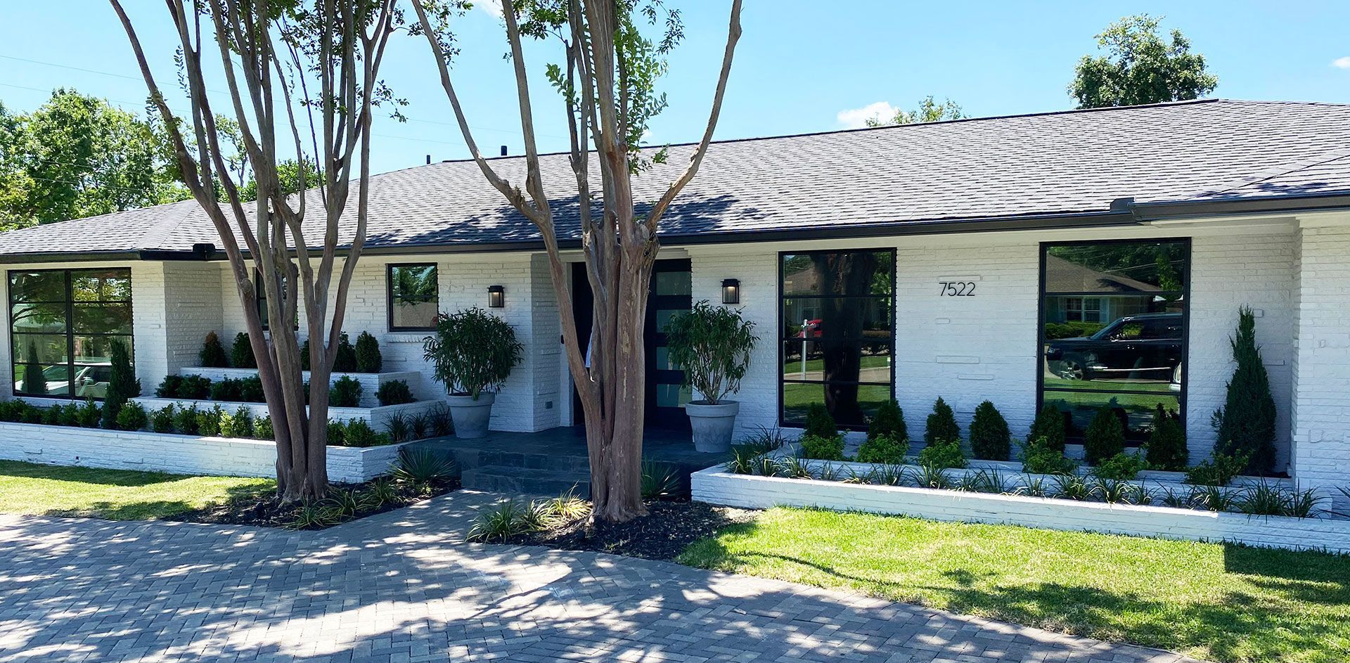 White brick house with black-framed windows, landscaped front yard, and trees.