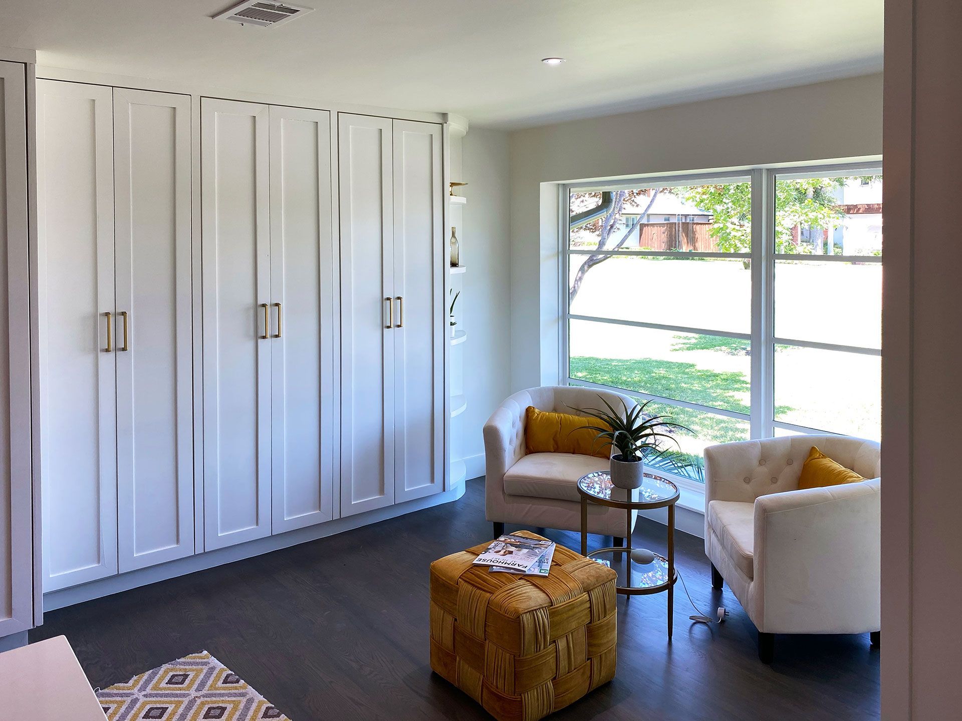 White cabinets, chairs, and ottoman in a room with a window, brown floors, and gold accents.