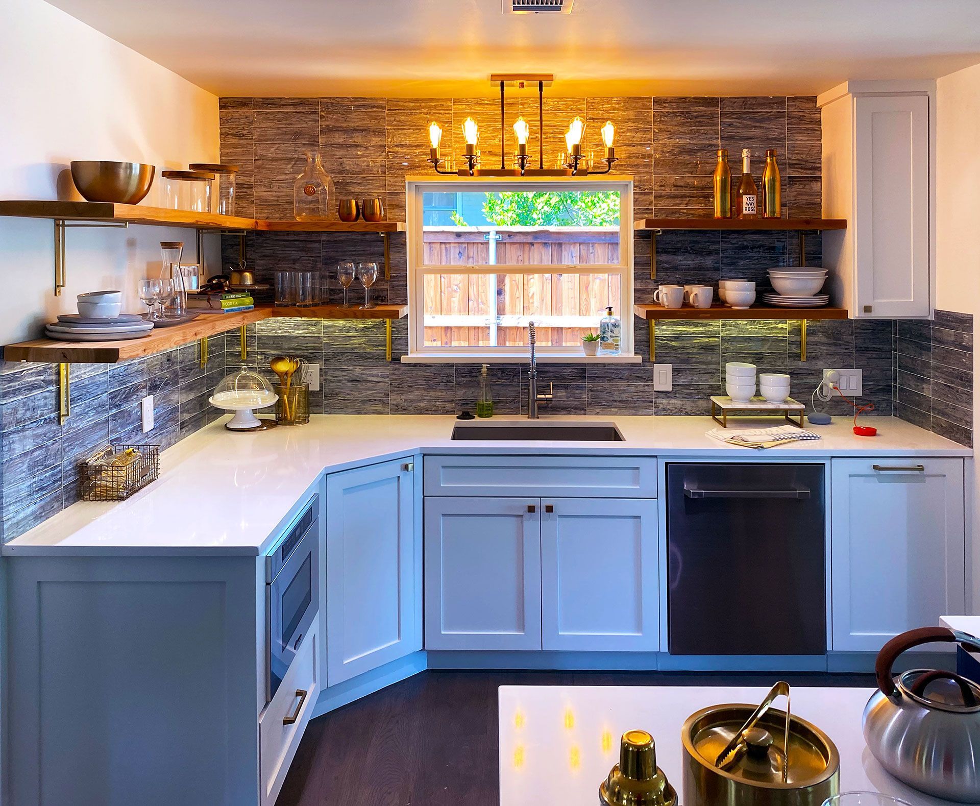Modern kitchen with white cabinets, stone backsplash, wooden shelves, and a window.
