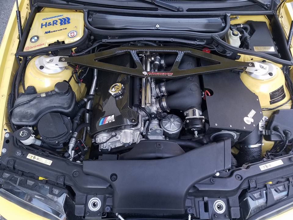 The engine of a yellow bmw is shown with the hood open.