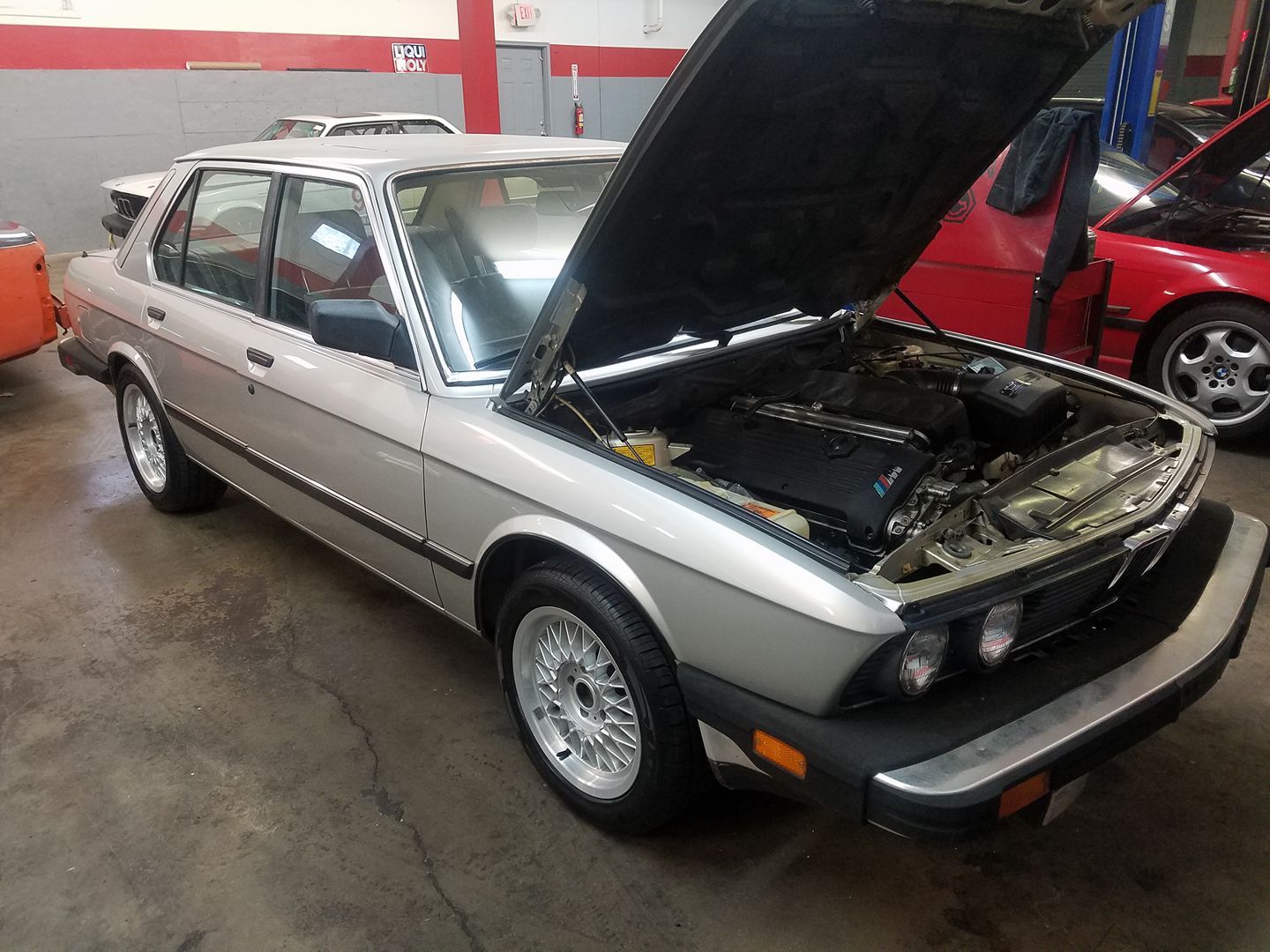 A silver car with the hood up in a garage
