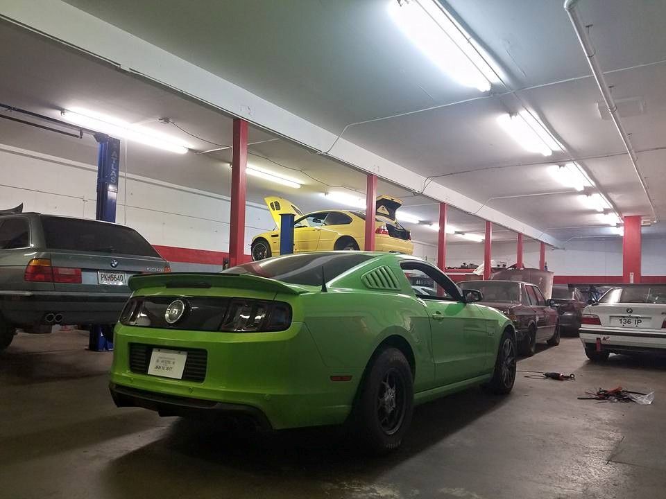 A green mustang is parked in a garage with other cars.