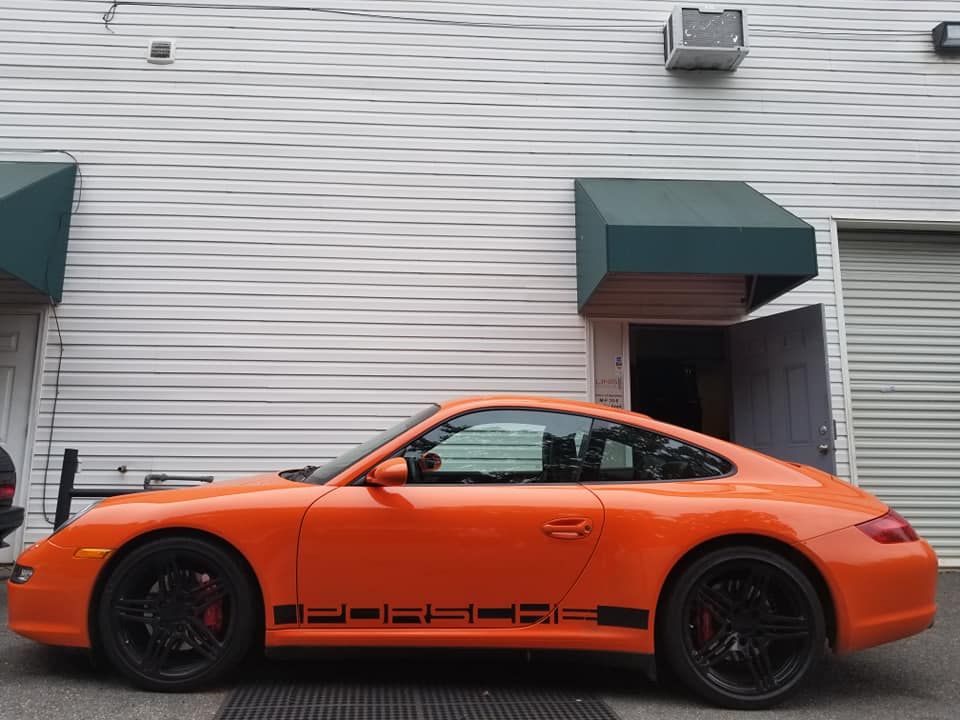 An orange porsche is parked in front of a white building