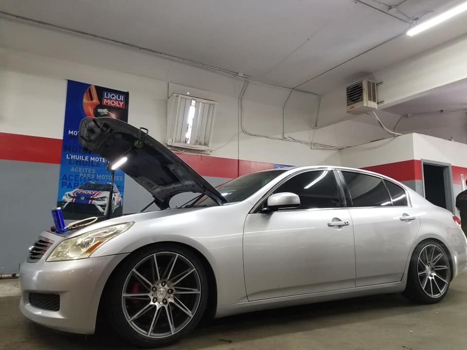 A silver car with the hood up is parked in a garage.
