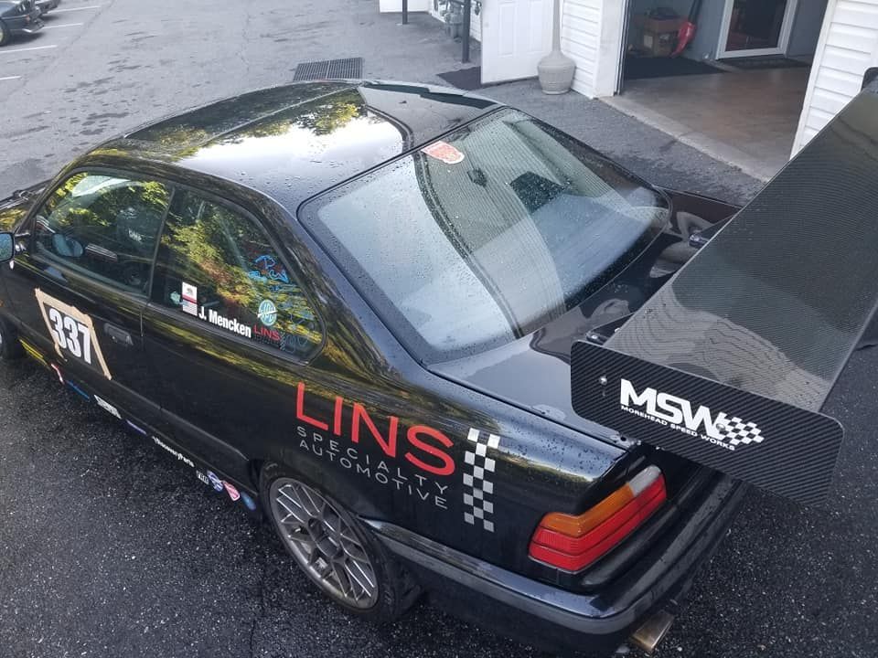 A black car with a spoiler on the back is parked in a parking lot.