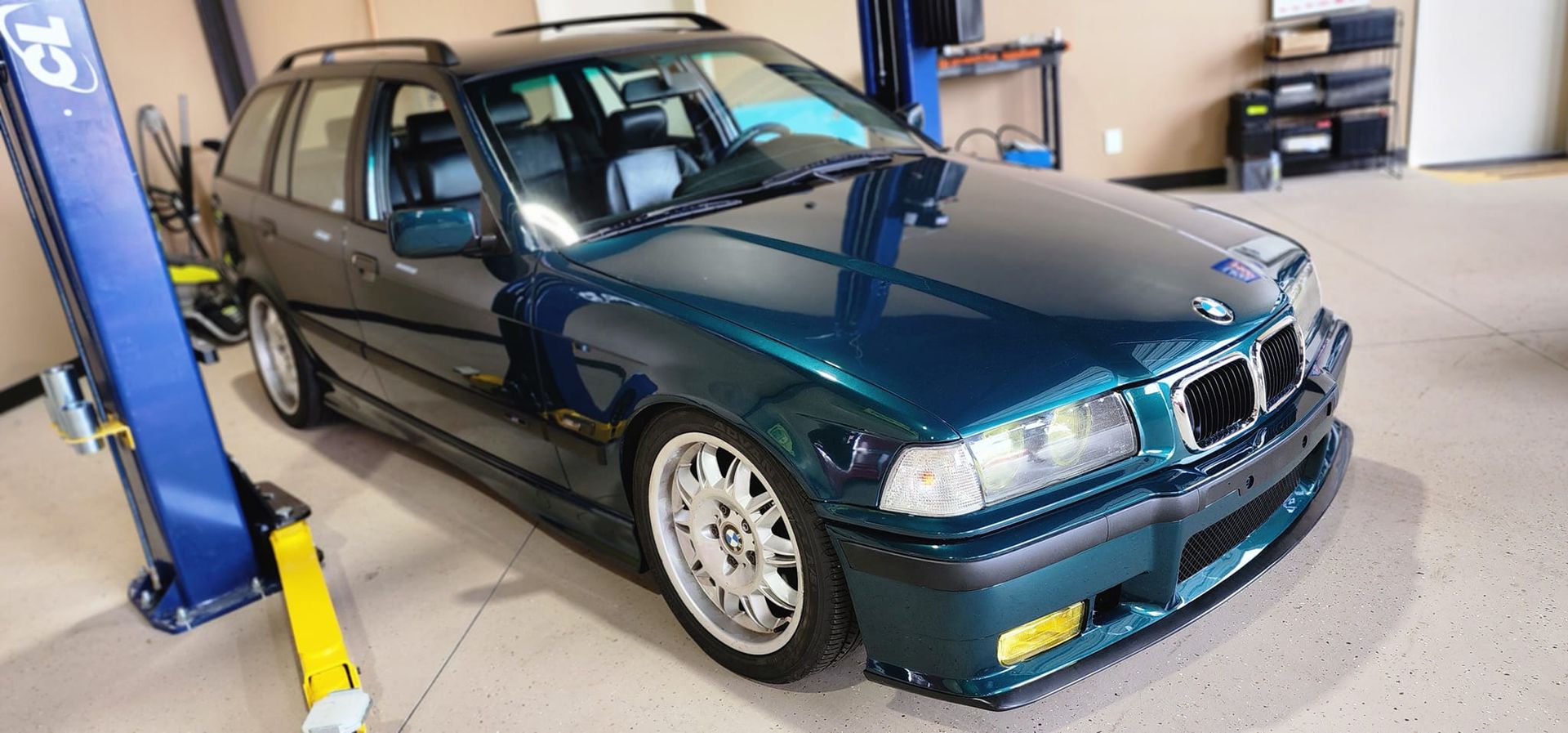 A green bmw is parked on a lift in a garage.