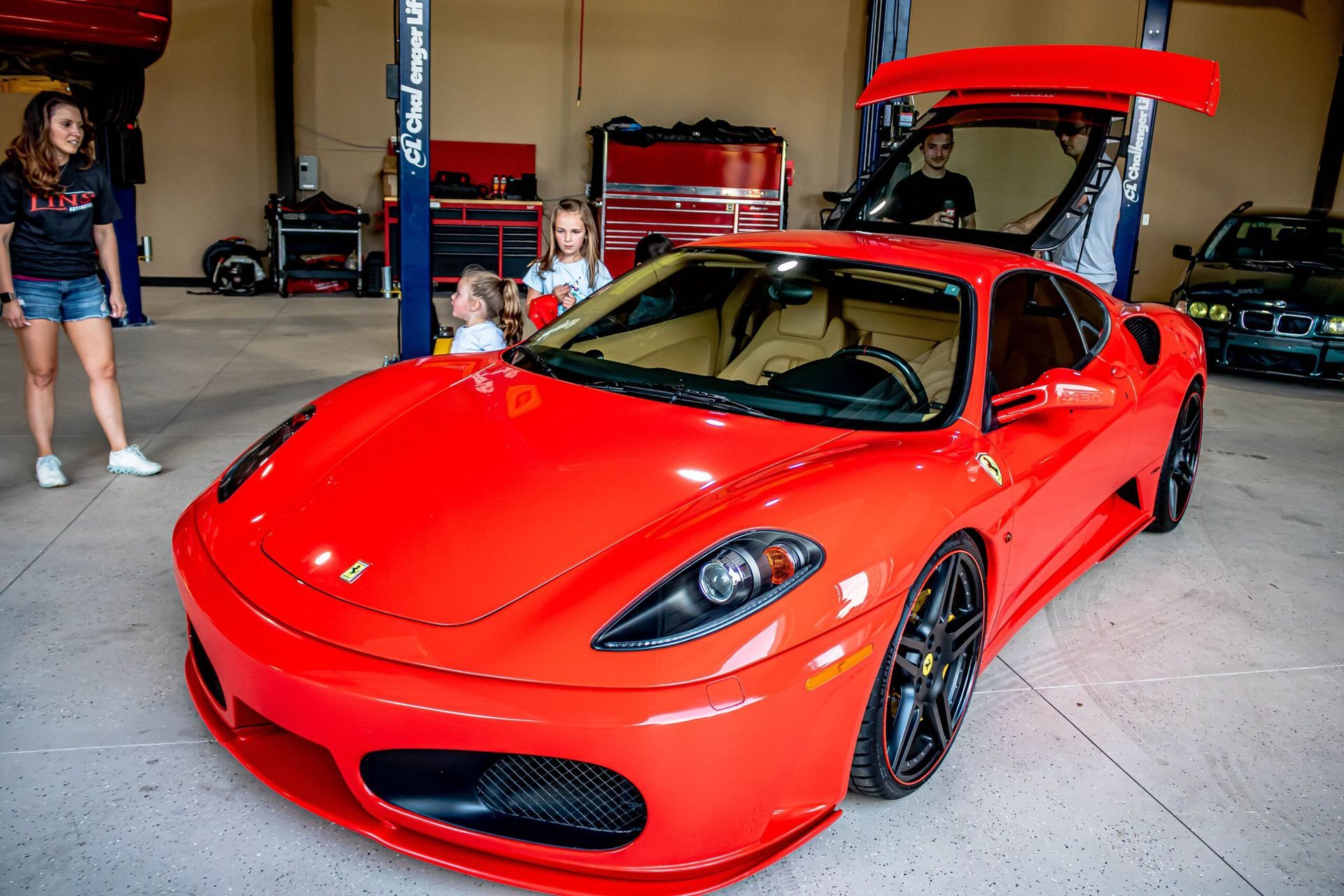 A red ferrari is parked in a garage with people standing around it