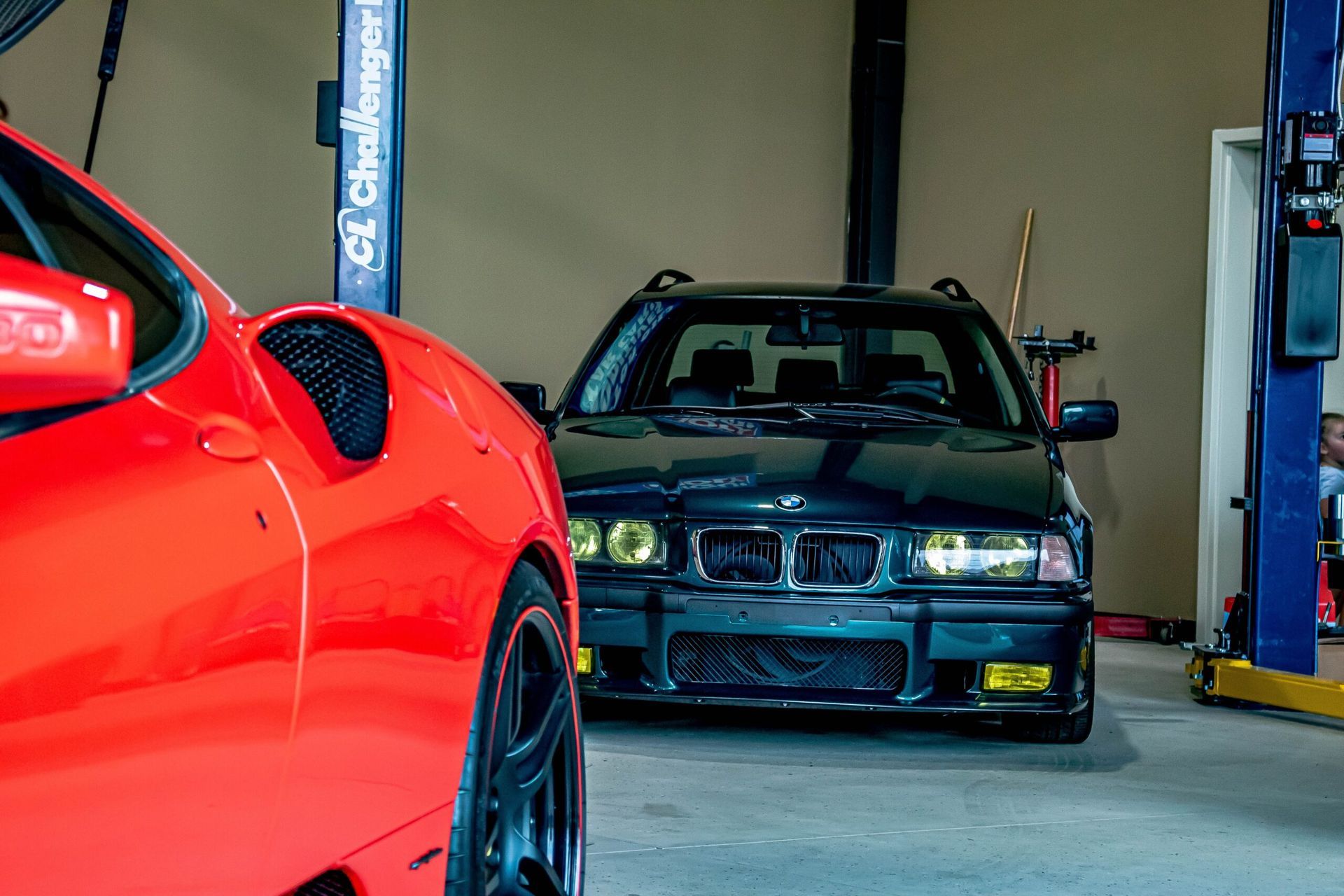 A red car is parked next to a black car in a garage.