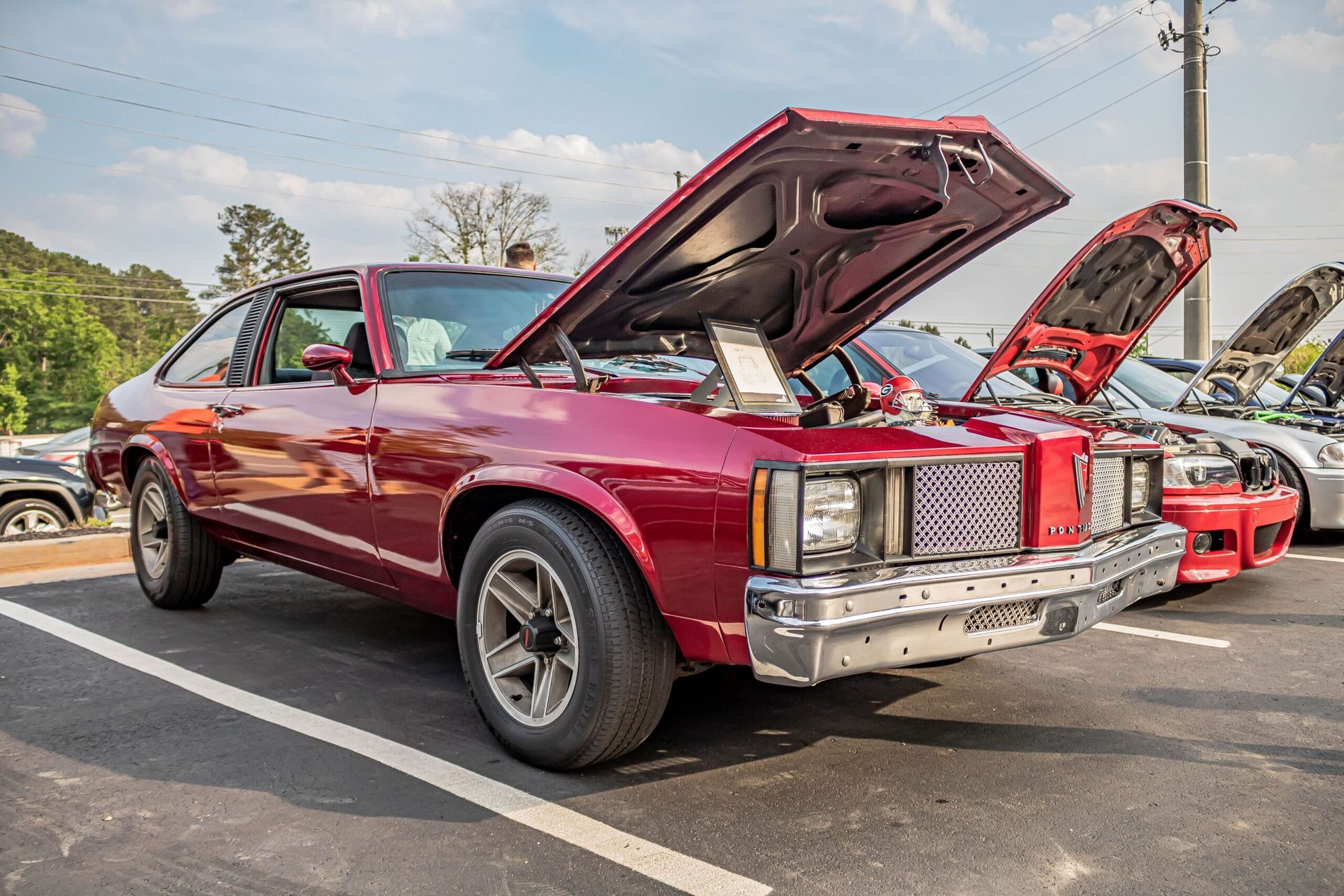 A red car with its hood up is parked in a parking lot.