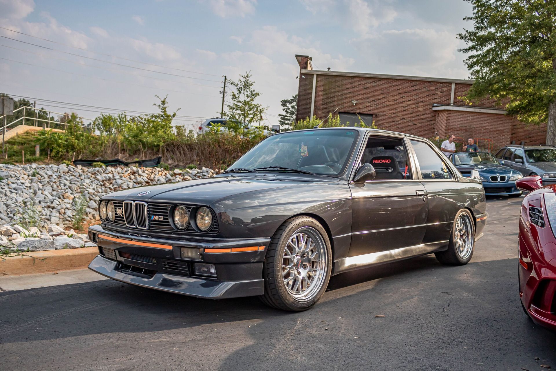 A black bmw is parked in a parking lot next to a red car.