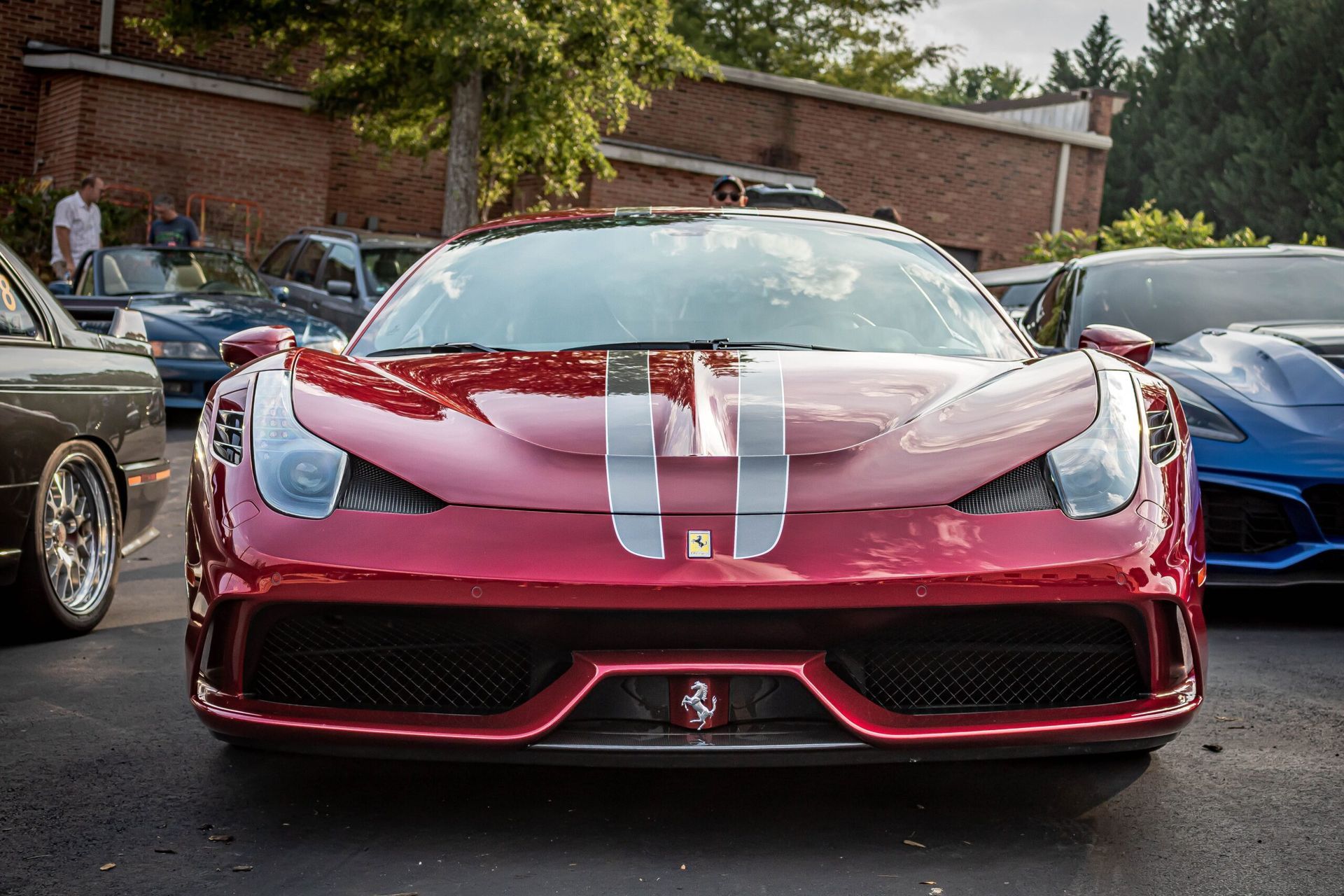 A red ferrari is parked in a parking lot next to other cars.