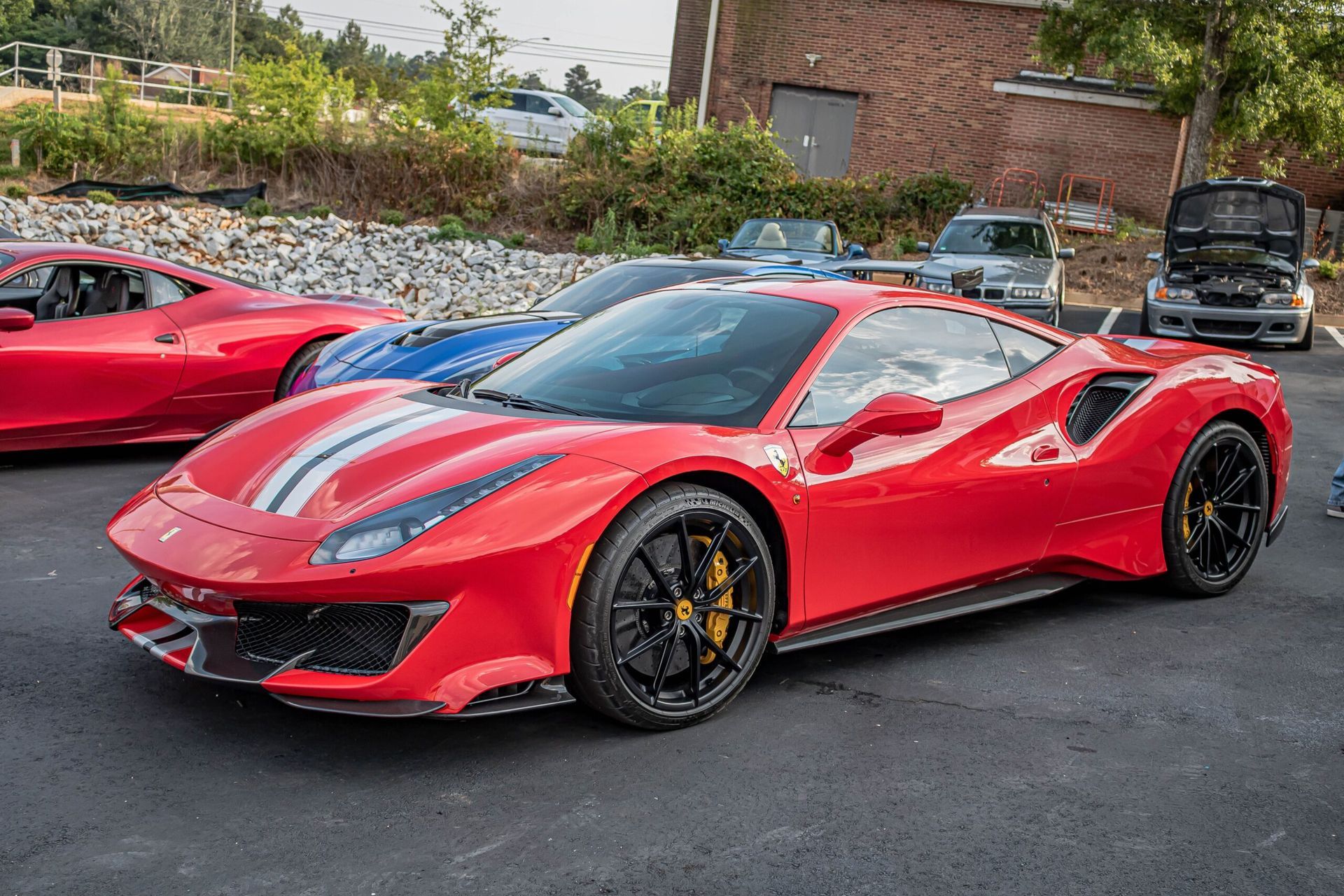 A red ferrari 488 pista is parked in a parking lot next to other cars.