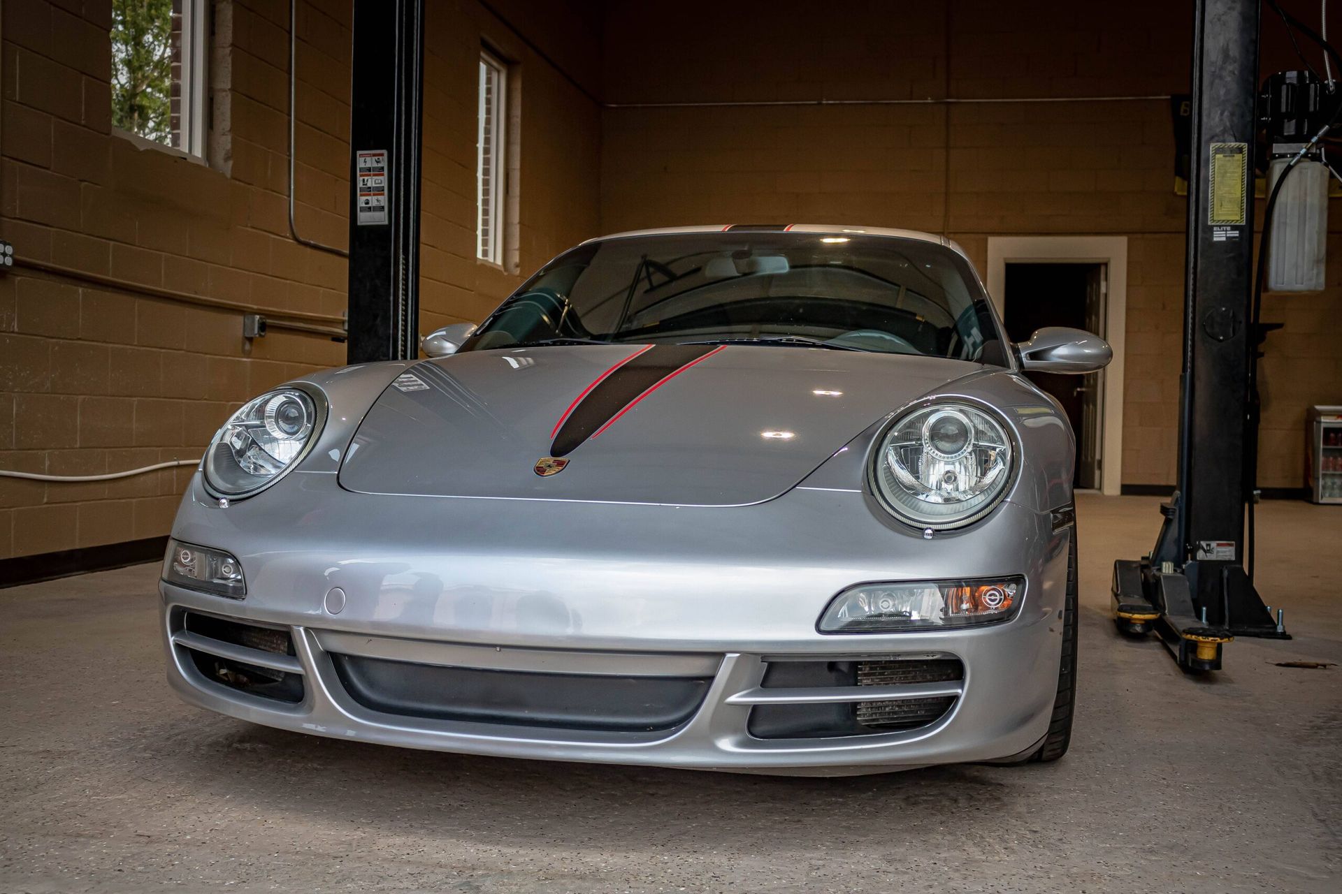 A silver porsche 911 is parked on a lift in a garage.