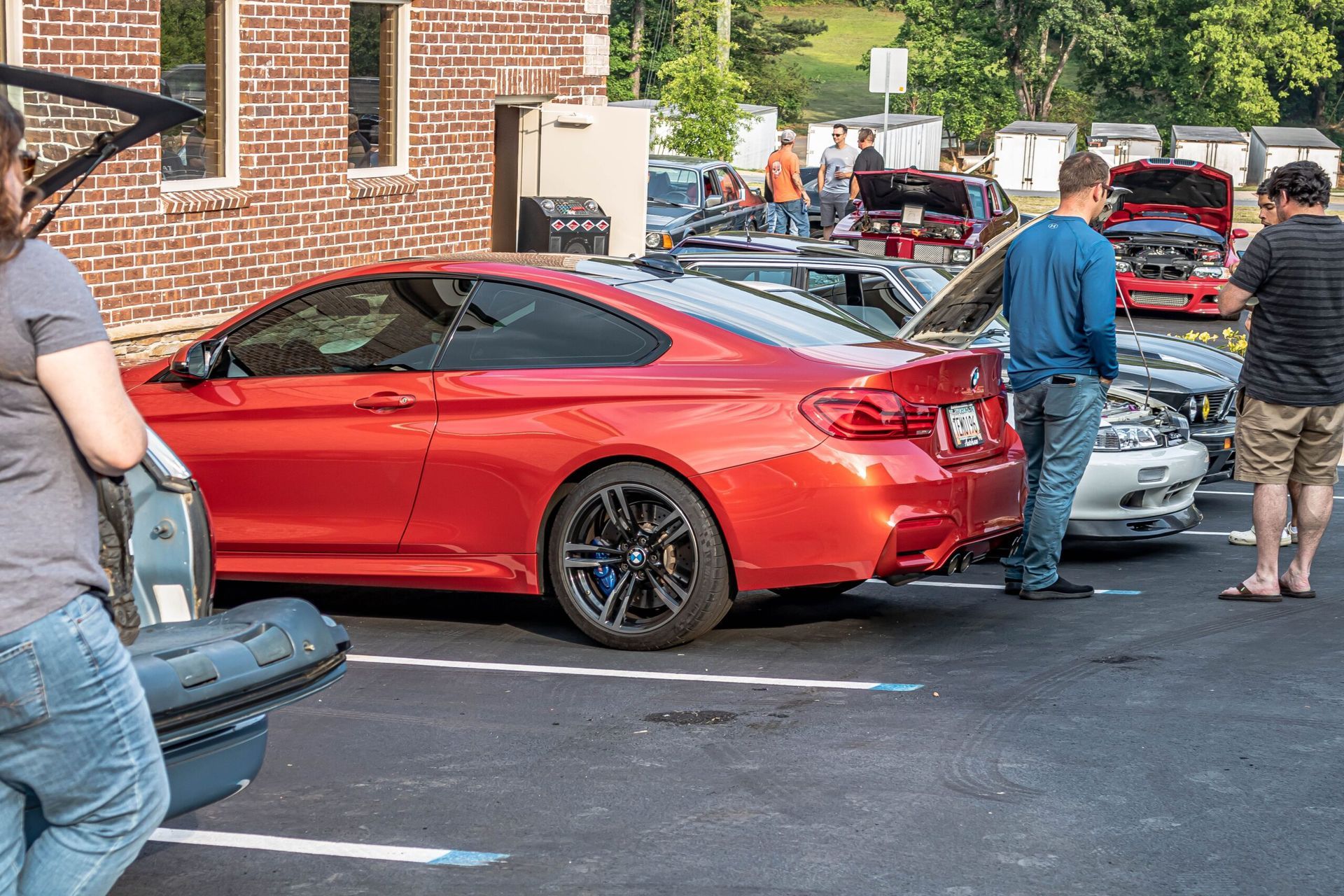 A group of people are standing around a row of cars in a parking lot.