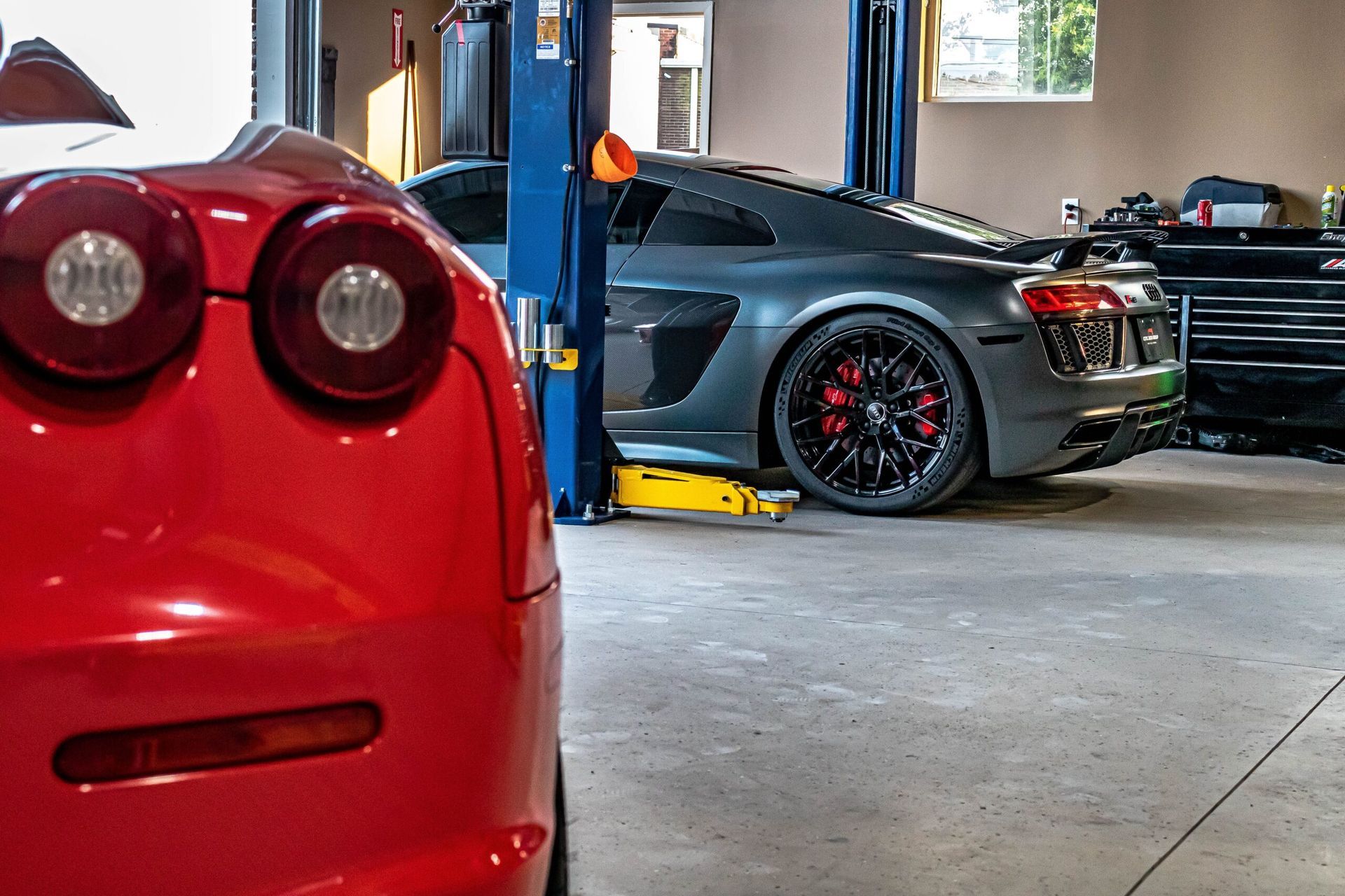 A red car is parked next to a gray car on a lift in a garage.