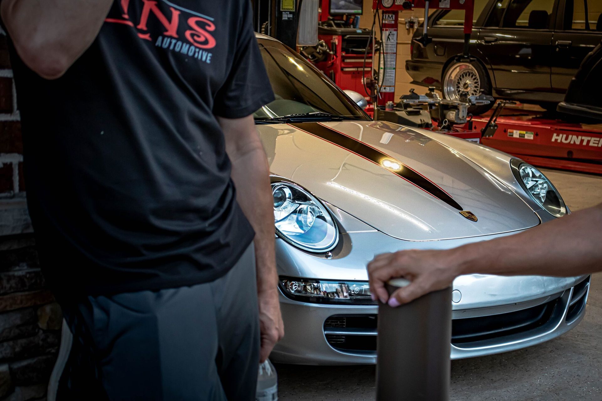 A man in a black shirt is standing next to a silver sports car.
