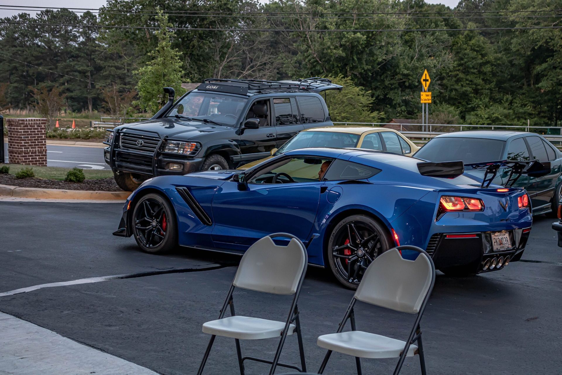 A blue sports car is parked in a parking lot next to two folding chairs.